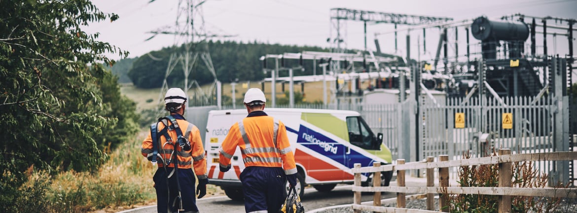 National Grid engineers walking towards their van with a pylon and electrical substation seen in the background